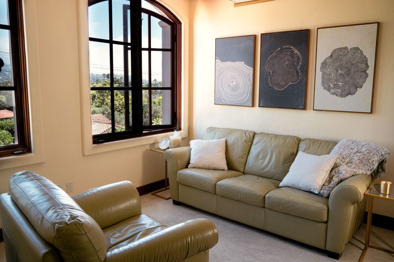 Sunlit therapy office with leather seating and an arched window overlooking the Santa Barbara hills